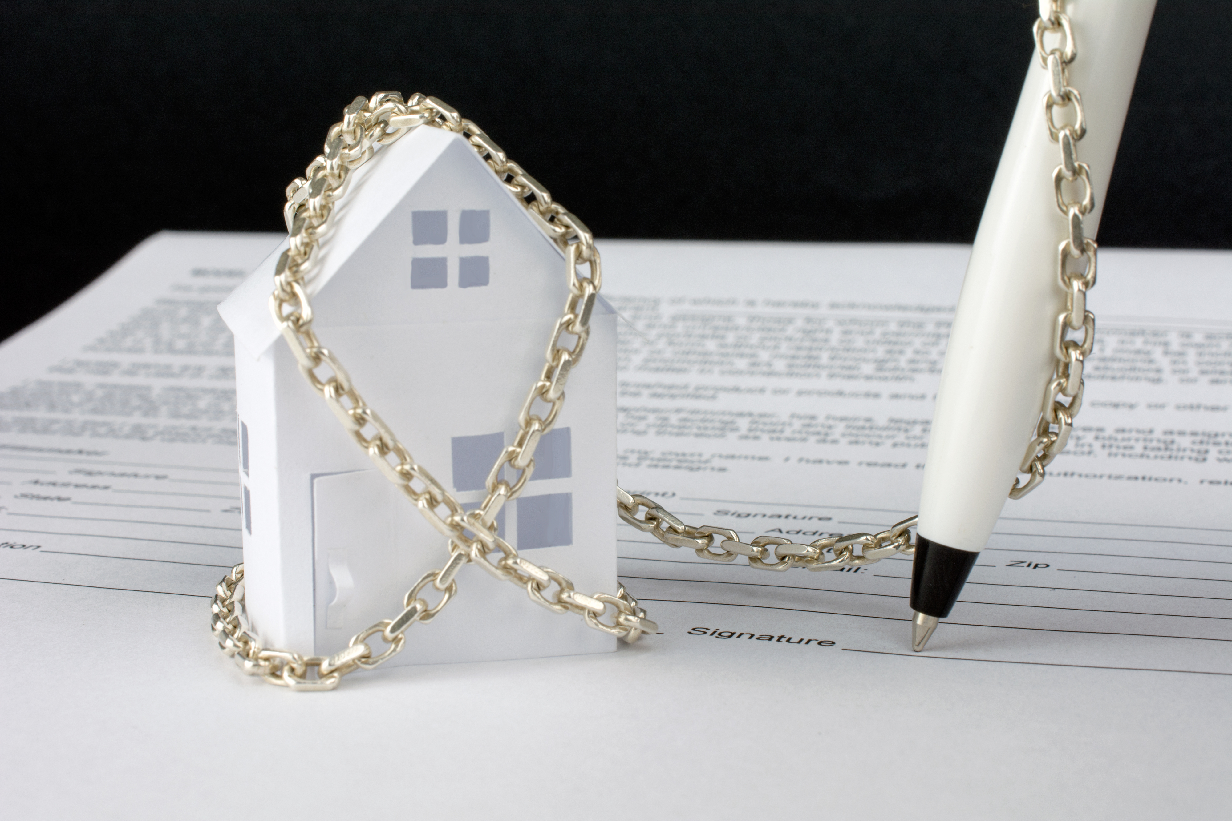 Paper house model chained and secured on tax documents with a pen, symbolizing IRS asset seizure and financial protection.
