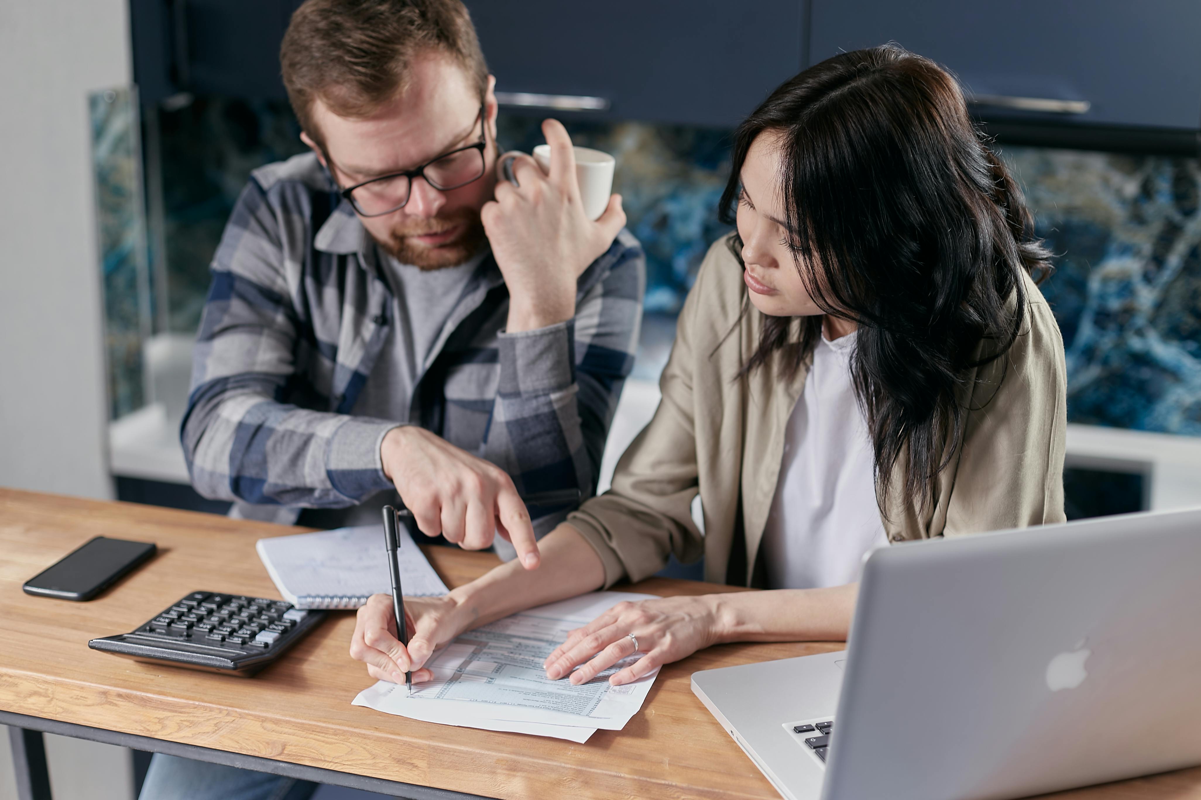 Individuals reviewing tax documents and discussing financial matters at a desk with a laptop and calculator, emphasizing tax resolution and IRS debt management.