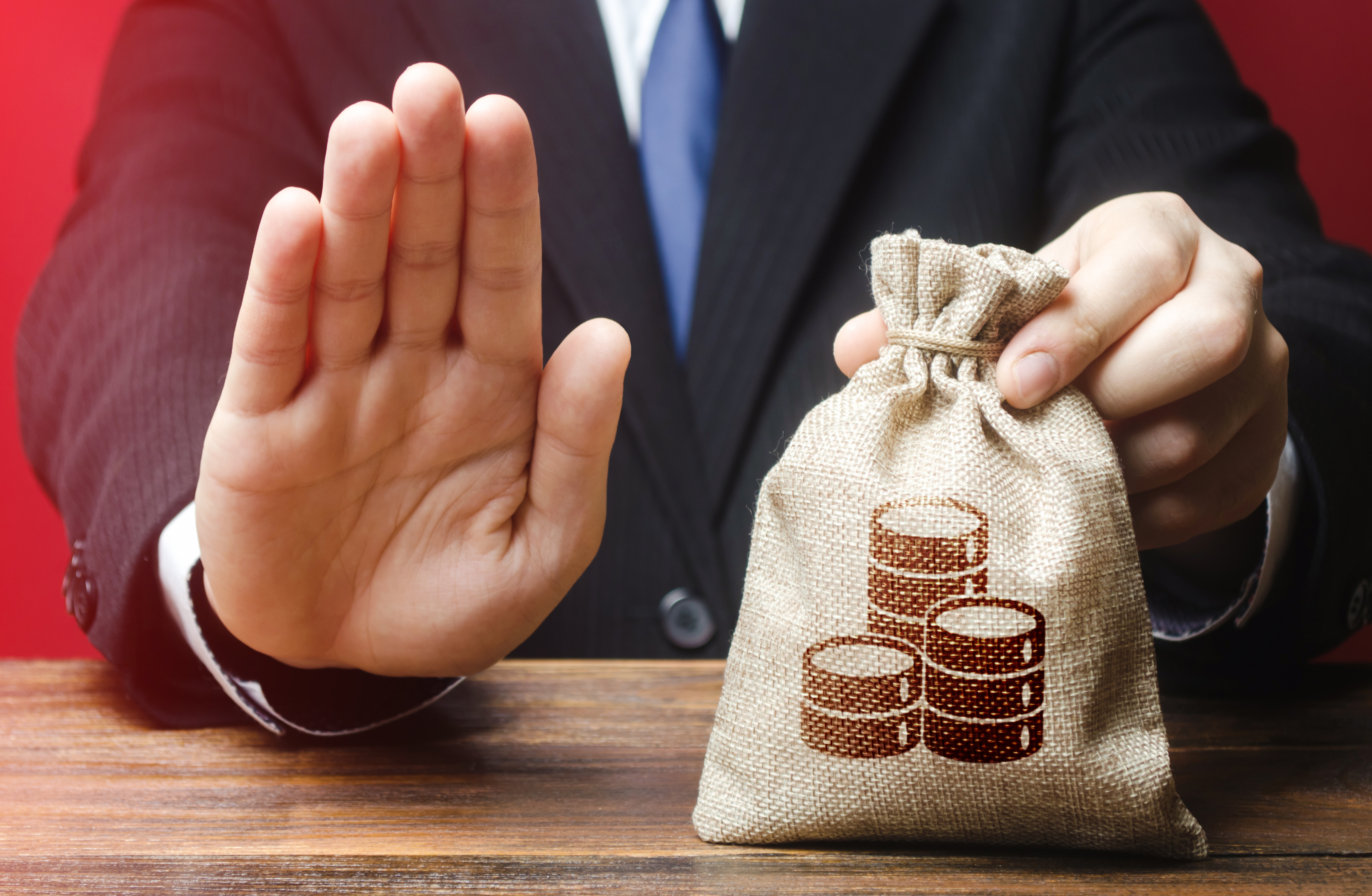 Businessman in suit holding a money bag with coins and raising hand to indicate stopping an IRS bank levy.