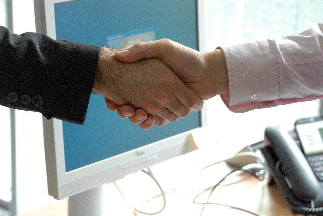 Handshake between two individuals in a professional setting, symbolizing partnership and trust, with a computer monitor in the background, relevant to tax attorney services and legal representation.