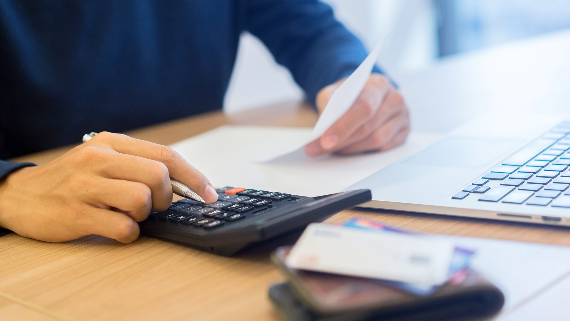 Person using a calculator and reviewing tax documents on a laptop, emphasizing the importance of professional tax assistance for resolving IRS and state tax issues.